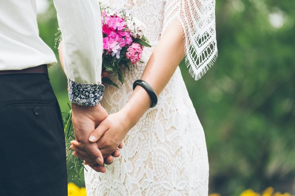 Sepasang pengantin bergandengan tangan dengan korsase merah muda